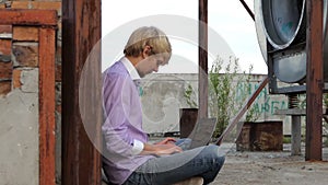 Blond man sits on a construction place and works at his laptop