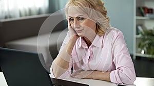 Blond middle-aged woman feeling bored watching online video, falling asleep