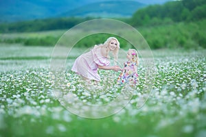 Blond mother with cute little daughter wearing white colourful pink dresses in chamomile field, summer time Enjoying spending time