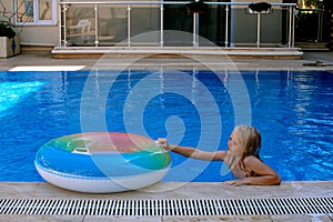 Blond preschool girl playing with float in the swimmimg pool on a beautiful summer day.