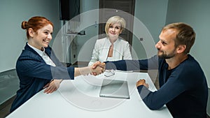Blond, red-haired woman and bearded man dressed in suits in the office. Business people shake hands making a deal in a