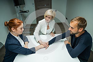 Blond, red-haired woman and bearded man dressed in suits in the office. Business people shake hands making a deal in a