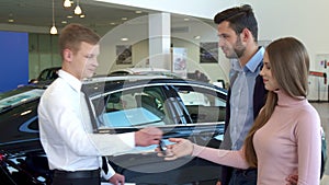 Salesman gives the car key to the couple at the dealership