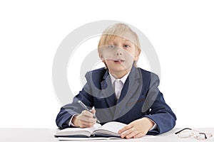 Blond schoolboy sits at a desk with a pen and listens attentively to the teacher. First grader in class. Education concept