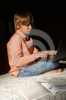 Blond serious boy spending time with notebook, sitting on the floor