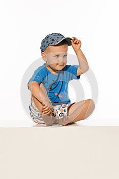 Blond smiling boy sitting on the table wearing baseball cap