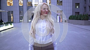 Blond smiling caucasian businesswoman walking on the city street and smiling. Young professional going for lunch.