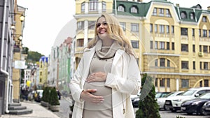 Blond stylish mother-to-be stroking belly, childbirth expectation, happiness