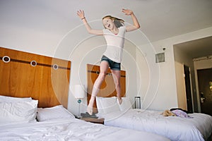 A blond teen girl jumping on beds in a hotel.