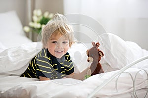 Blond toddler child in bed with stuffed monkey, playing in the morning