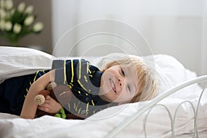 Blond toddler child in bed with stuffed monkey, playing in the morning