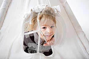 Blond toddler child, plaing in teepee with stuffed monkey