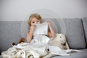 Blond toddler child, wiping his nose in a tissue, sneezing and coughing