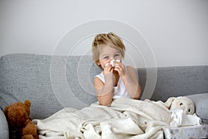 Blond toddler child, wiping his nose in a tissue, sneezing and coughing