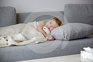 Blond toddler child, wiping his nose in a tissue, sneezing and coughing