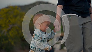 Blond toddler holds mother hand walking on beach at twilight