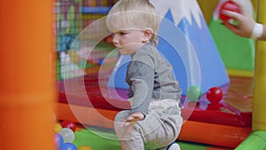 Blond toddler plays with little balls on playground