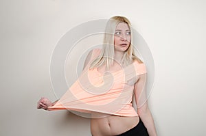 Blond woma leaning on white wall, wear a crop top and shorts