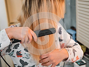 blond woman in the bathroom straightens her hair with a curling iron