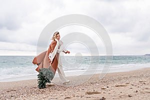 Blond woman Christmas tree sea. Christmas portrait of a happy woman walking along the beach and holding a Christmas tree