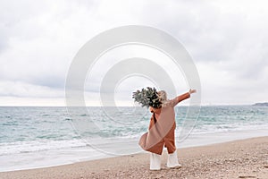 Blond woman Christmas tree sea. Christmas portrait of a happy woman walking along the beach and holding a Christmas tree