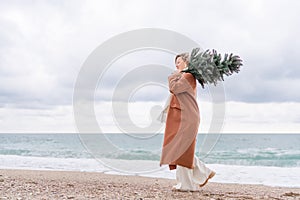 Blond woman Christmas tree sea. Christmas portrait of a happy woman walking along the beach and holding a Christmas tree