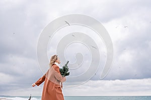 Blond woman Christmas tree sea. Christmas portrait of a happy woman walking along the beach and holding a Christmas tree