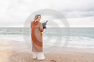 Blond woman Christmas tree sea. Christmas portrait of a happy woman walking along the beach and holding a Christmas tree