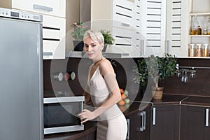 Blond woman cooking with a microwave in kitchen