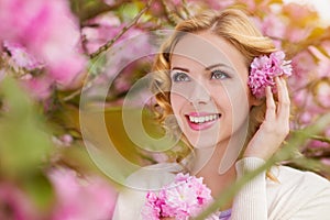 Blond woman, curly hair against pink tree in blossoom