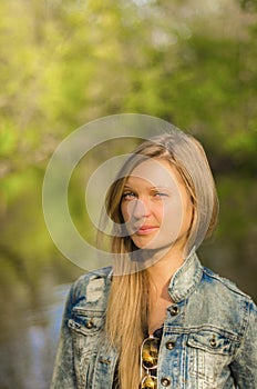 A blond woman in a denim jacket on the background of nature looks with disbelief. Suspicious look