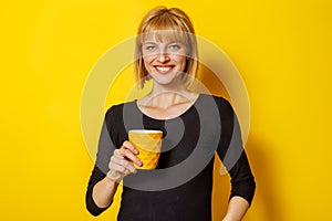 Blond woman drinking coffee on yellow color background