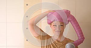 Blond woman drying her hair with hair drayer pink