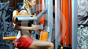 The blond woman on the equipment gym trains the obliques