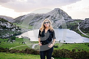 Blond woman in front of the camera wearing casual clothes in a mountainous landscape with lake