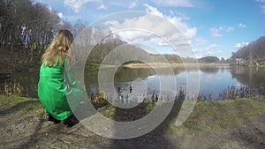 Blond woman with green coat feeding duck birds near lake. 4K