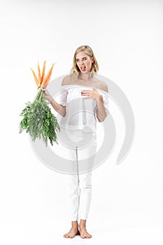 Blond woman holding carrot with green leaves on white background. girl feels bad from carrots and diets