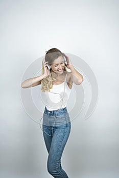 Blond woman holding her headphones with both hands listening to music smiling white  background