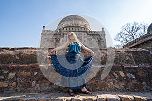 Blond woman holds up her long maxi skirt, posing in front of an ancient temple, Lodi Garden in New Delhi India