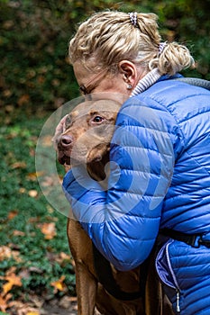 Blond woman hugging two toned brown Doberman mix rescue dog, outside in nature