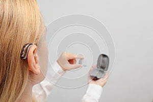 Blond woman Inserts Hearing Aid on ear at home. Deafness treatment, hearing solutions. Deaf woman wearing hearing aid. Digital