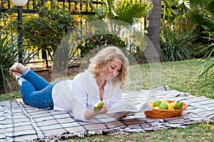 Blond woman lies on a blanket in the garden and reads a book