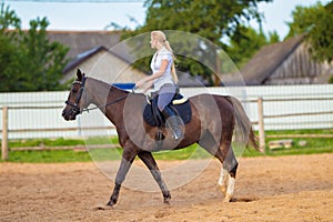 Blond woman with long hair jockey rider on a bay horse, in a paddock on a ranch