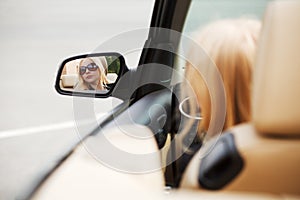 Blond fashion woman looking in the car mirror