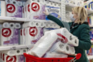 A blond woman in a medical mask buys a lot of toilet paper in a supermarket. Panic and deficiency during the coronavirus pandemic