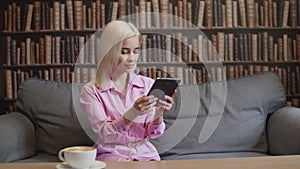 Blond woman in pink shirt is reading ebook in cafe