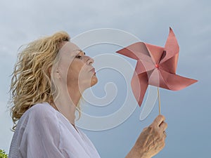 A blonde woman plays with a red pinwheel by blowing to make it spin