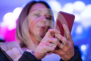 Blond woman portrait using mobile at night, with neon city lights background.