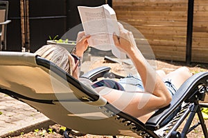 Blond woman reading book by taking sunbath in the house backyard