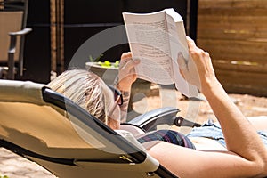 Blond woman reading book by taking sunbath in the house backyard